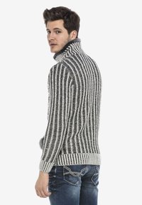Grijs en wit gestreepte gebreide trui met een hoge kraag, voorzien van een textuurafwerking. Draagt met blauwe jeans, die een aansluitend ontwerp laten zien.