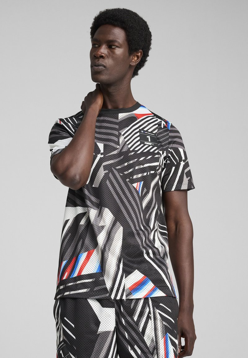 Czarna koszulka z krótkim rękawem, z geometrycznym wzorem w odcieniach szarości, bieli, czerwieni i niebieskiego; siateczkowa tekstura oraz okrągły dekolt z logo.