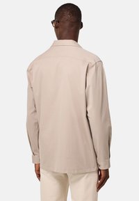 Camicia beige a maniche lunghe con colletto casual. Tessuto morbido, taglio dritto e dettagli dei polsini con bottoni. Indossata con pantaloni chiari.