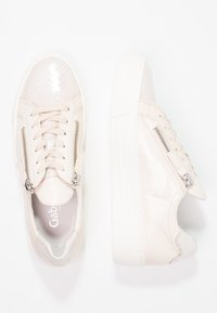 Baskets beige clair avec une finition brillante et texturée. Elles présentent des fermetures éclair métalliques, une semelle en caoutchouc et un bout lisse. Design élégant.