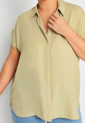 Blusa verde oliva chiaro in tessuto liscio. Presenta un colletto, maniche corte e una patta con bottoni. Orlo arrotondato con spacchi laterali.