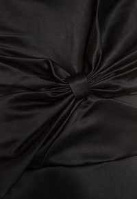 Svart satin tyg med en knuten design i mitten, som har en mjuk textur och subtil glans, vilket skapar mjuka draperingar och konturer.