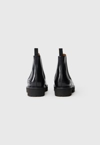 Bottines chelsea en cuir noir avec une finition lisse, des côtés élastiques et des languettes, dotées d'une semelle en caoutchouc texturée pour une meilleure adhérence.