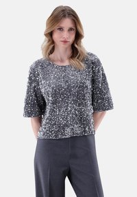 Kurzärmliges graues Top mit Pailletten und rundem Halsausschnitt, mit einer strukturierten Oberfläche und einem lässigen Schnitt, kombiniert mit dunklen Hosen.