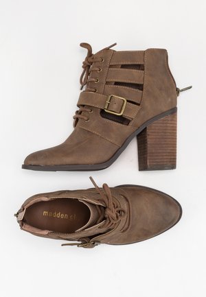 Bottines marron avec un look texturé, dotées d'un talon empilé, de lacets et d'une sangle décorative avec boucle. Accents de couleur bicolore visibles.