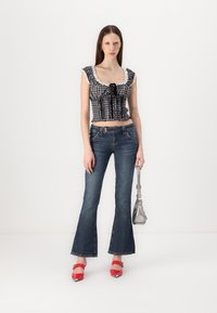 Plavi karirani kratki top s čipkastim obrubom, uparen s tamnim zvonastim trapericama. Model nosi crvene štikle i drži srebrnu torbicu.