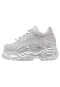 Srebrne sneakersy na platformie z błyszczącą cholewką, okrągłym noskiem i grubą podeszwą. Wyróżniają się sznurowadłami oraz akcentem logo na boku.