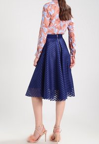 Marinblå, midilång kjol med vertikalt randigt mönster, tillverkad av textilmaterial. Kombinerad med en mönstrad persikofärgad blus och ljusa skor.