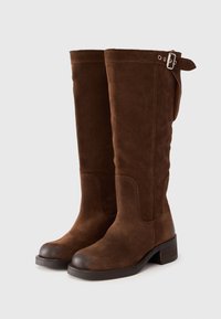 Brown suede knee-high boots with a rounded toe, low block heel, and silver buckle detail on the side. Smooth texture throughout.