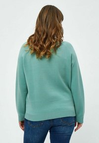 Maglione verde menta a costine con maniche lunghe e una vestibilità rilassata. Tessuto morbido e orlo arrotondato, abbinato a jeans blu.
