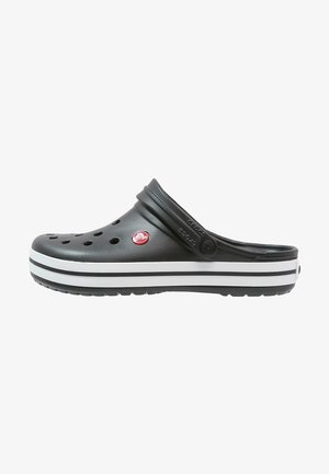 Sabot Crocs noir avec des trous de ventilation, un logo circulaire rouge, une semelle rayée blanche et noire, et une bride de talon ajustable.