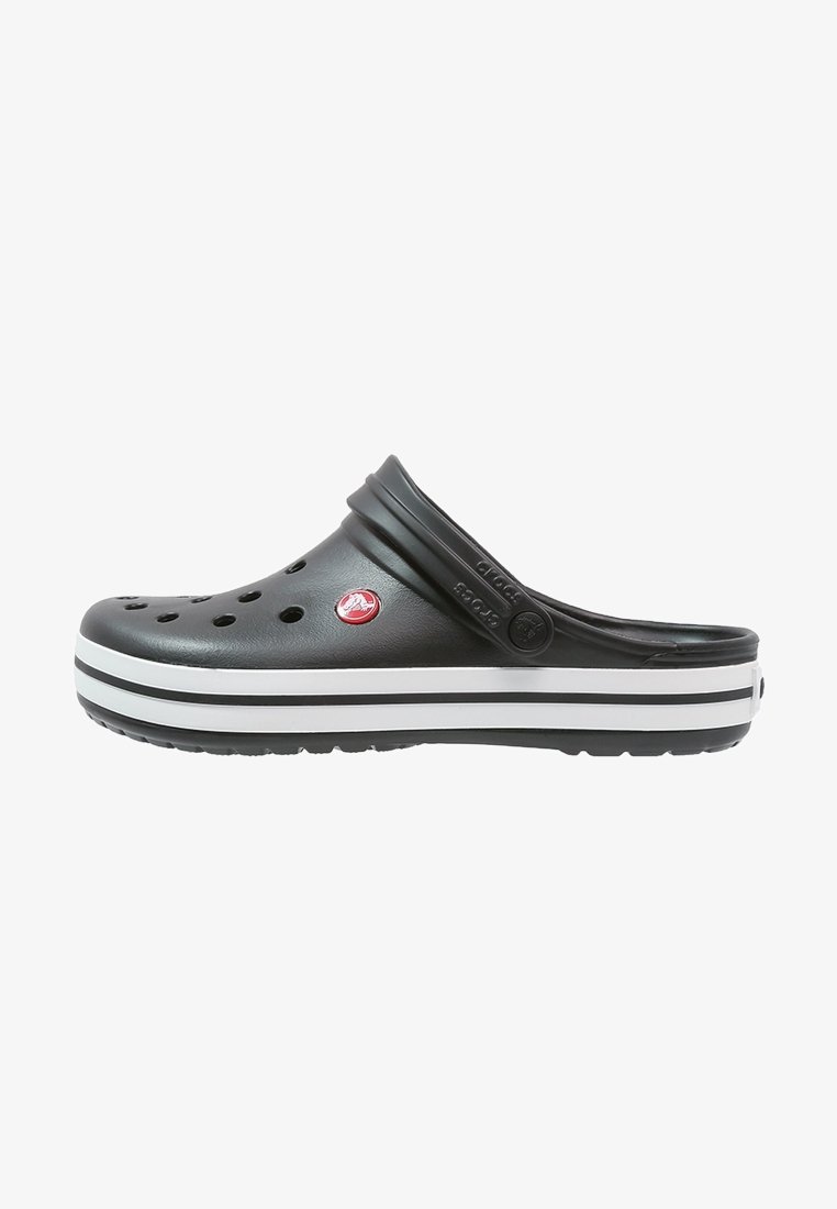 Sabot Crocs noir avec des trous de ventilation, un logo circulaire rouge, une semelle rayée blanche et noire, et une bride de talon ajustable.