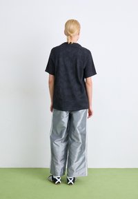 Zwarte T-shirt met korte mouwen en een gestructureerde afwerking, gecombineerd met brede zilverkleurige broeken met zijstrepen, en zwart-witte schoenen.