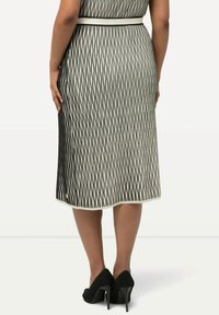 Knie-lange jurk met een zwart-wit verticale zigzagpatroon, een aansluitende taille met een witte riem, en een zijsplit. Gepaard met zwarte hakken.