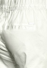 Pantaloni in tessuto bianco con cintura elastica, dotati di una singola tasca applicata sul retro e una texture sottile. Nessun motivo o accessorio visibile.