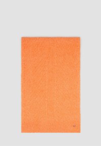 Couverture tricotée orange avec une texture côtelée verticale. Matière douce avec un petit logo dans le coin, forme rectangulaire.