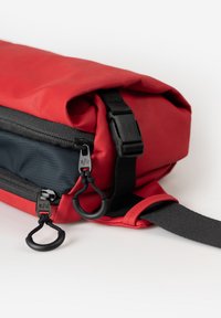 Borsa impermeabile rossa con cima arrotolata, zip nere e tracolla removibile. Presenta hardware regolabile e anelli per attacchi.