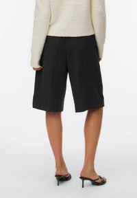 Mørkegrå skreddersydde shorts laget av lett stoff, knelange med en strukturert design og rene kanter, sammen med en kremfarget genser og hælsandaler.