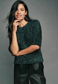 Maglione verde morbido a maglia con maniche corte, tessuto testurizzato, scollatura rotonda, abbinato a pantaloni in ecopelle nera. Finitura liscia e lucente.