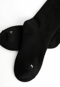 Schwarze Baumwollsocken mit gerippter Textur, die verstärkte Zehenbereiche und kleine weiße Größenmarkierungen auf den Sohlen aufweisen.