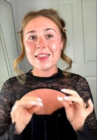 Haut en dentelle noire avec manches transparentes, présentant un design découpé. Le mannequin a la peau claire, les cheveux coiffés et de longs ongles, exprimant un geste avec les mains.