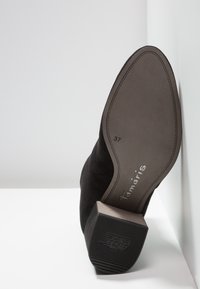 Semelle d'une botte cheville en daim noir avec talon carré, indiquant la taille 37, la marque "Tamaris" et le motif "ANTISLIDE" sur le talon.