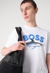 Camiseta blanca con letras azules "BOSS" y un gráfico de marlín, combinada con un bolso negro texturizado con un asa suave.