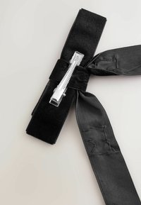 Must mustriba mustriba hõbe metalli klamber; omadab tekstuuriga pinda, millel on sile satiinstribade detail, mis on seotud ühelt poolt kaareks.