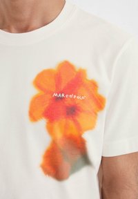White cotton t-shirt featuring a large, vibrant orange and red flower print with a soft texture and "MARCO POLO" logo in white.