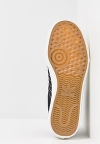 Černá podešev tenisky s vzorem z gumové pryže pro trakci, bílé detaily a texturované prvky, včetně koncentrických kruhů a vlnitých drážek.