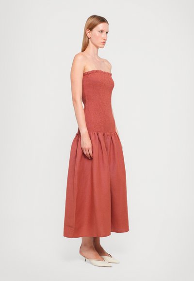 Rustfarget stroppeløs kjole med smocket liv, volangdetalj og en luftig, lang skjørt laget av lett stoff.