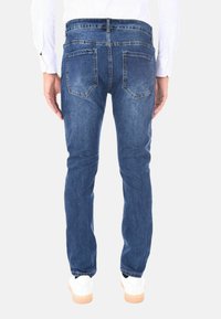 Jeans in denim blu scuro con design a gamba dritta, tasche posteriori visibili e vita classica, abbinati a sneakers bianche.