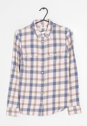 Chemise à manches longues à boutons avec un motif à carreaux bleu et beige, deux poches poitrine à l'avant, suspendue sur un cintre noir sur un fond blanc.