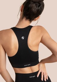 Schwarzer Sport-BH mit Racerback-Design, glatter Textur und dezentem Branding. Der elastische Bund am unteren Ende bietet Unterstützung und Komfort.