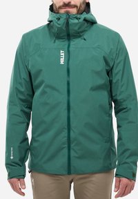 Veste imperméable verte avec capuche, fabriquée en matériau Gore-Tex. Elle dispose d'une fermeture éclair à l'avant, de poignets ajustables et d'un logo sur la poitrine.