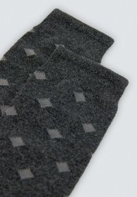 Calcetines grises con una superficie texturizada que presenta un patrón de diamantes en gris más claro. El diseño incluye dos secciones elevadas en la parte superior.