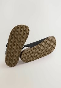 Sorte sandaler med en tekstureret gummisål, der har et zigzag-mønster. Materialet er blødt, og designet inkluderer justerbare remme.