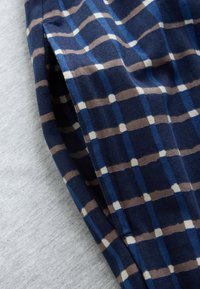 Tissu à carreaux bleu, marron et blanc plié sur une surface douce gris clair, montrant de près les détails de la texture et du motif.