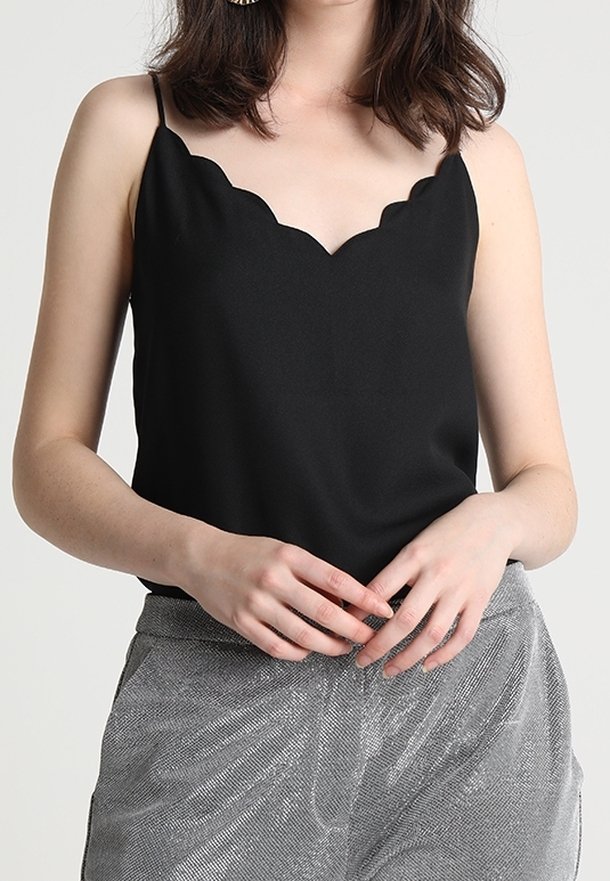 Camisole noire avec décolleté festonné, bretelles fines, texture lisse. Associée à un pantalon taille haute argenté texturé.