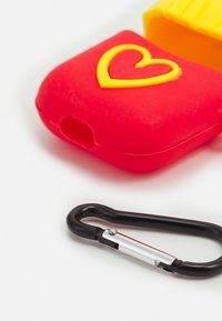 Red silicone case with a yellow heart design, featuring a black metal carabiner. Smooth texture and rounded edges. Yellow accent piece included.