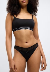 Juodas medvilninis braletė su plonais petnešėliais ir logotipo juosta; derinamas su atitinkančiomis juodomis kelnaitėmis su nėrinių apdaila ir maža kaspinėlio detale.