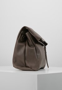 Borsa in pelle grigia con un design morbido. Presenta una parte superiore pieghevole, una tracolla con borchie e una texture liscia. Base arrotondata, hardware minimale.