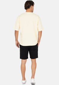 Geel katoenen T-shirt met korte mouwen en een losse pasvorm, gecombineerd met zwarte shorts. De outfit wordt compleet gemaakt met witte canvas sneakers.
