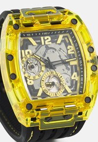 Transparente gelbe Kunststoffuhr mit großem rechteckigem Ziffernblatt, schwarzen Akzenten und doppelt vorhandenen Ziffernblättern; verfügt über auffällige Stundenmarkierungen und Chronographenfunktionen.