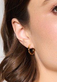 Złota skręcona kolczyka na uchu, z gładką fakturą i warstwowym wzornictwem, odbijająca światło dzięki połyskliwej powierzchni.