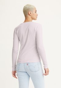Langärmliges, helllila Baumwollhemd mit rundem Halsausschnitt und taillierten Ärmeln, getragen mit hellblauen Jeans.