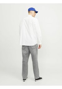 Biela košeľa s gombíkmi a uvoľneným strihom, šedé denimové nohavice a čierne tenisky. Modrá čapica dopĺňa outfit, pohľad zozadu.