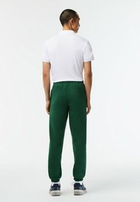 Pantalones deportivos verdes con cintura elástica y puños, combinados con una camiseta polo blanca de manga corta, mostrando la vista posterior.