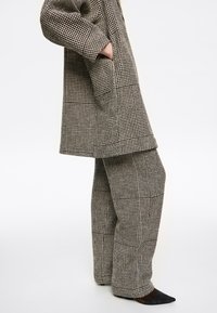 Czarnobiały, kratkowany płaszcz w połączeniu z luźnymi, kratkowanymi spodniami, wykonanymi z fakturowanej tkaniny. Płaszcz posiada boczne kieszenie i luźny krój.