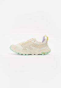 Beige Sport Schuh mit strukturiertem Mesh und Wildlederüberzügen, grünem Gummiaußensohle, lilafarbenem Akzent an der Ferse und gelbem Zugband. Mit Vibram-Branding.